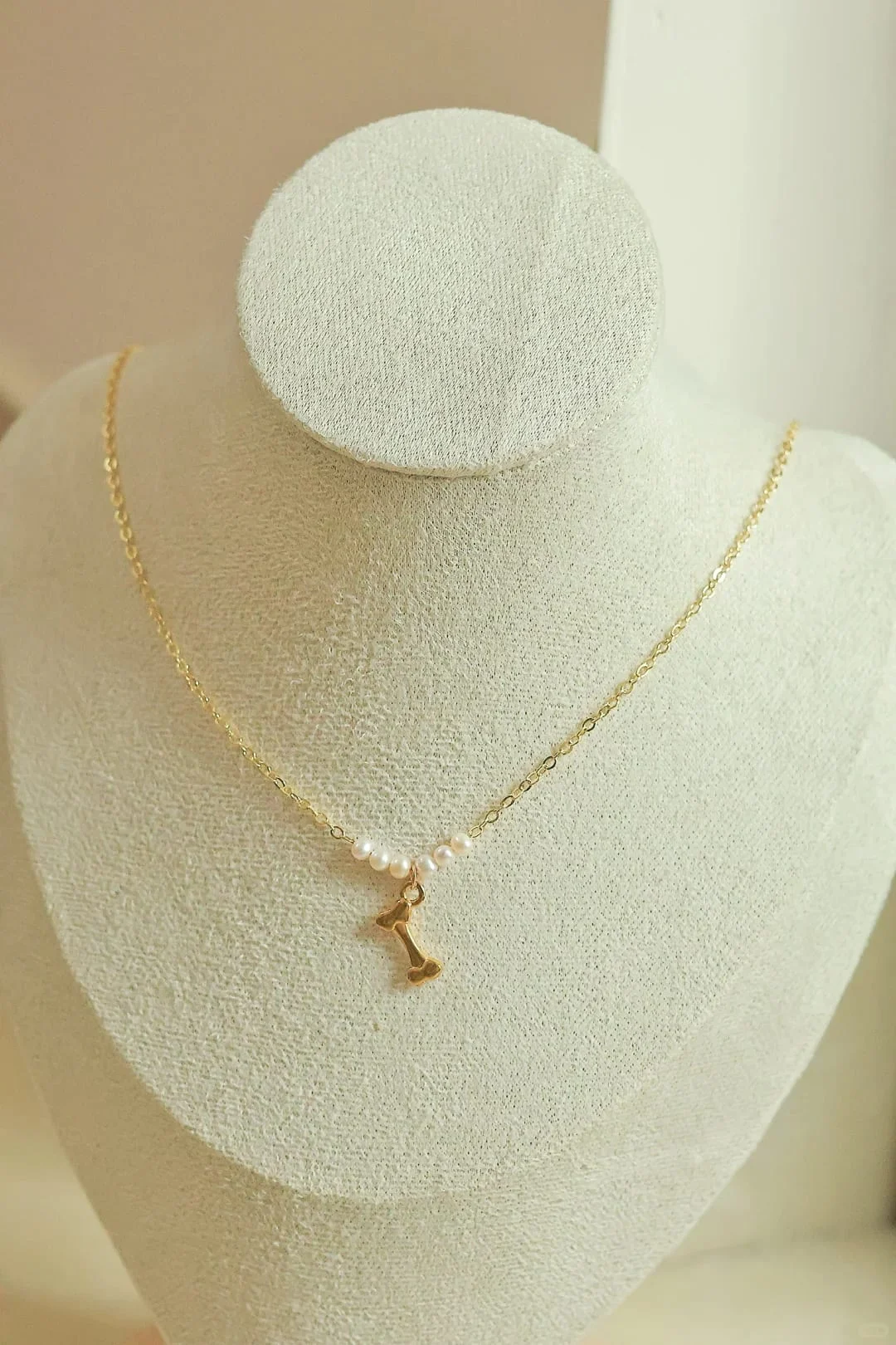 Fine gold-toned chain necklace on a display bust, with four small white beads and a gold-toned bone charm at the centre.