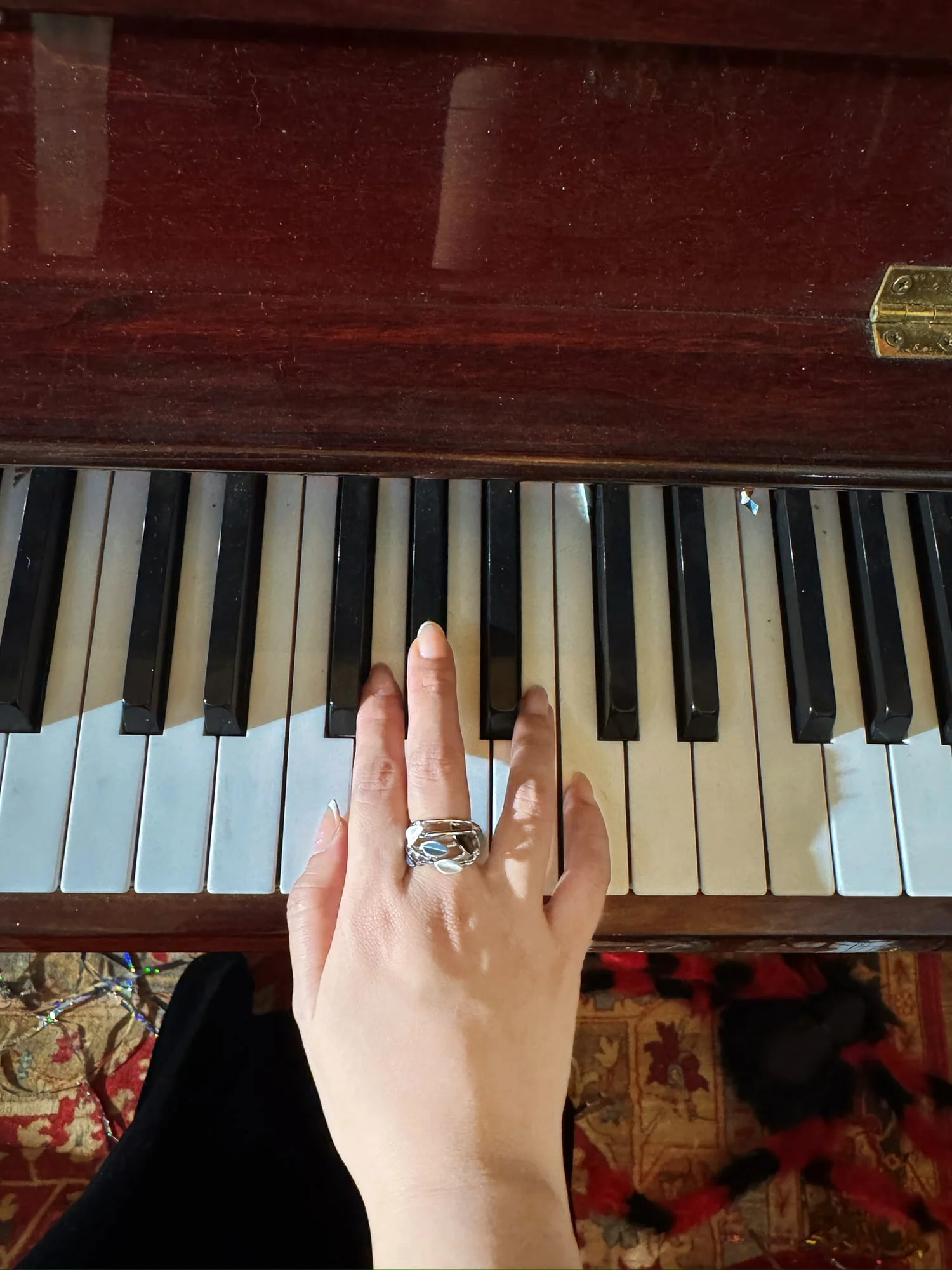 Hand wearing the wide silver-toned leaf ring with white enamel, photographed from above on piano keys.