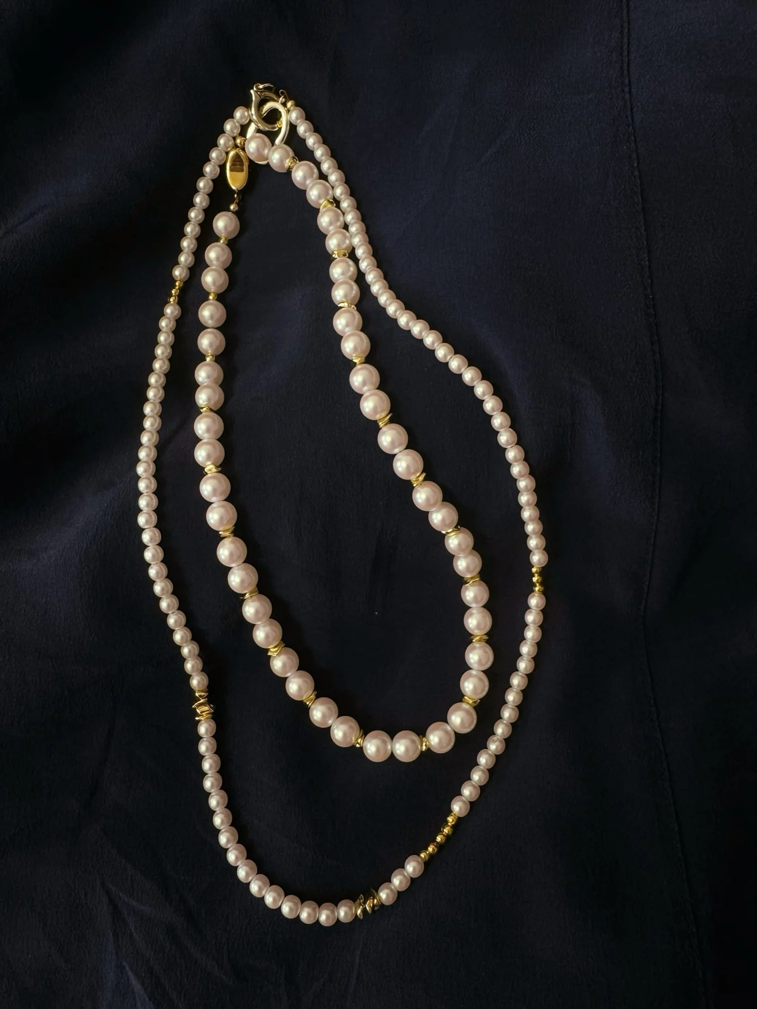 Two white-bead necklaces laid on navy fabric; this is the single strand with larger beads and a lobster clasp.