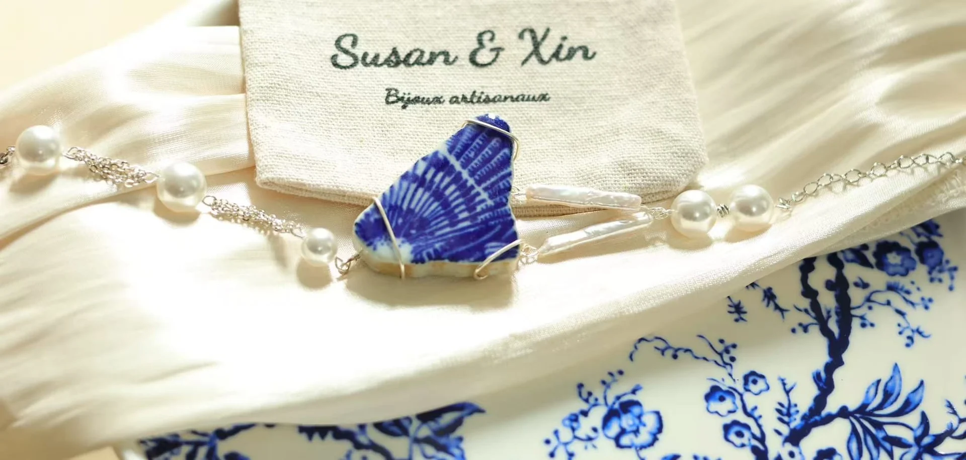 The same shard bracelet laid horizontally on white satin in front of a Susan&Xin pouch, the fan pattern on the fragment clearly visible.