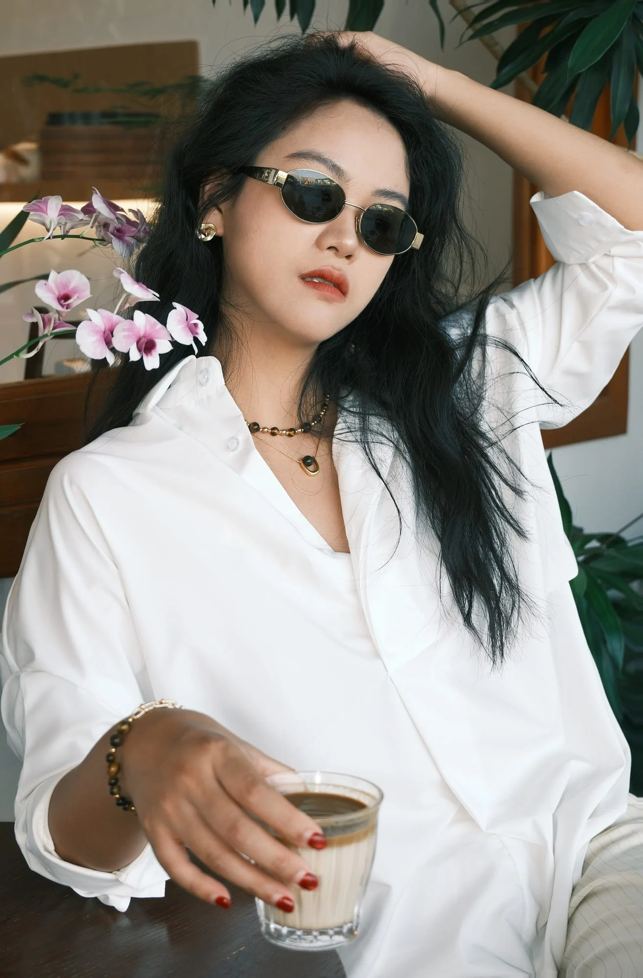 The half-chain bead bracelet on the wrist of a model holding a coffee: half brown banded beads, half gold-toned paperclip chain.