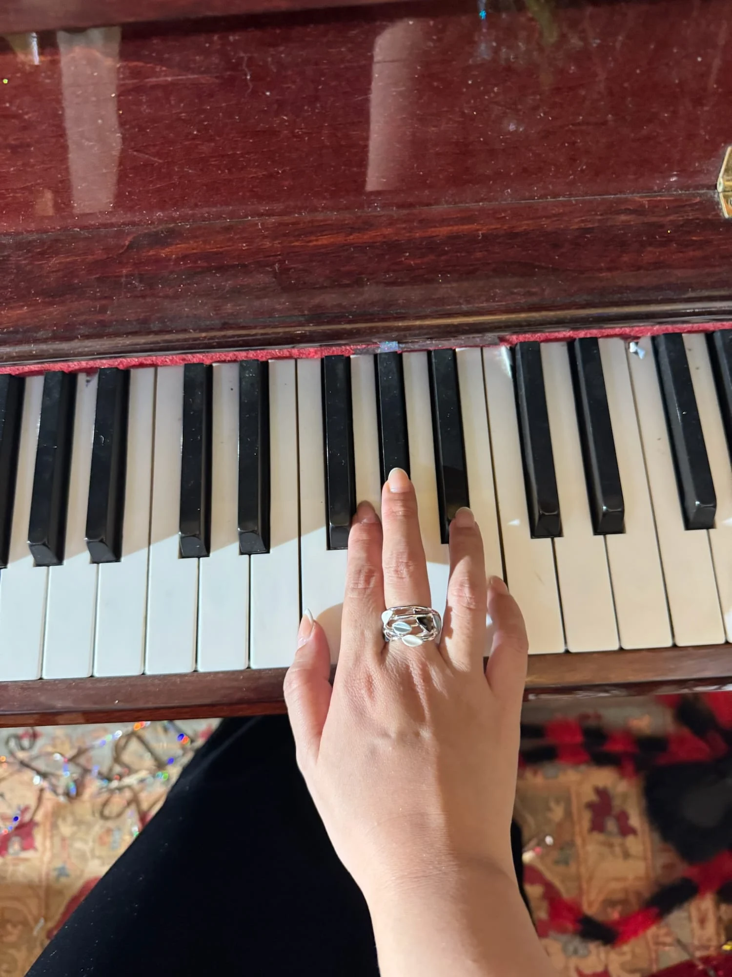 A second overhead photograph of the same silver-toned leaf ring on piano keys.
