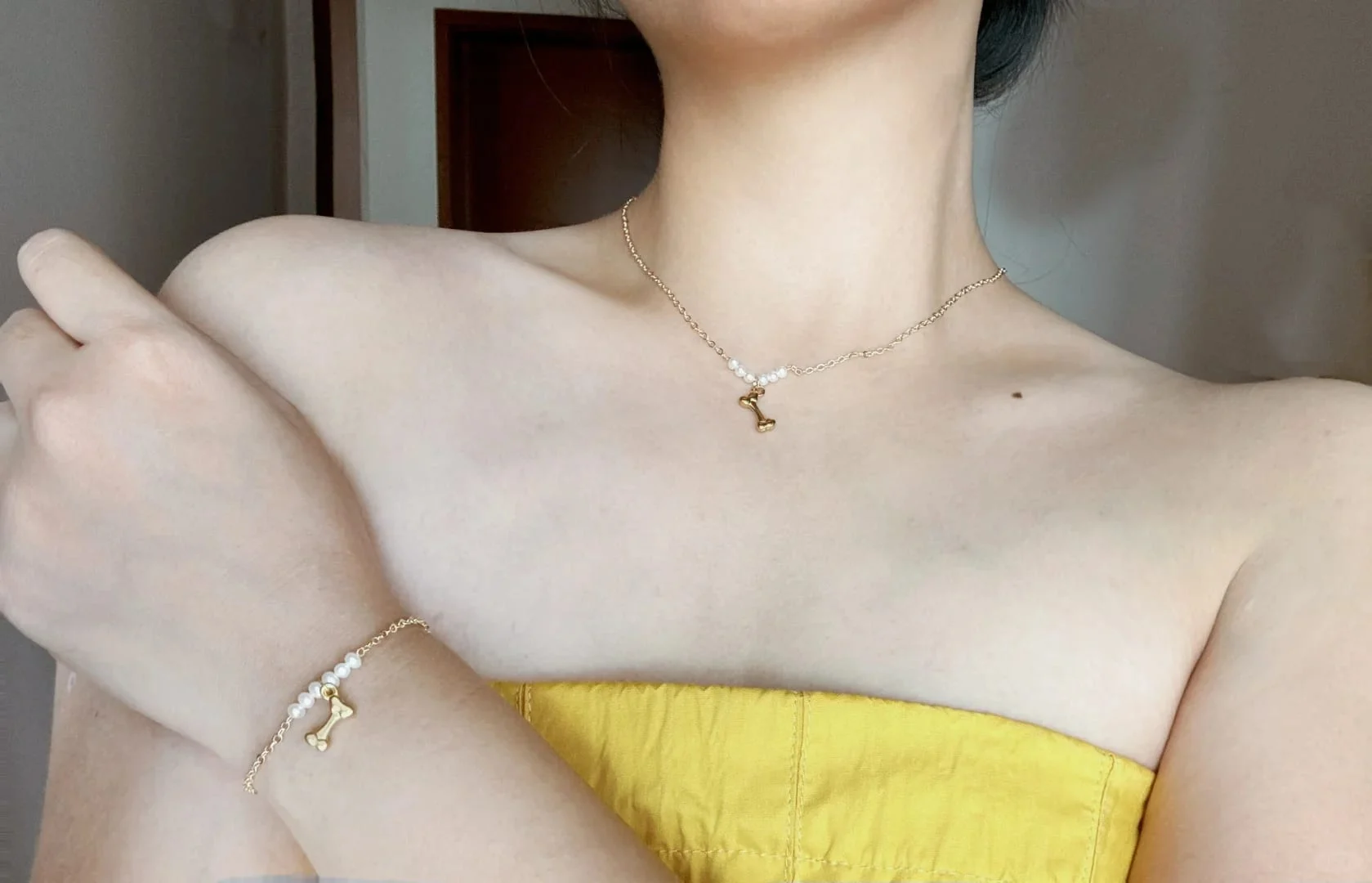 Model in a yellow strapless top wearing the gold-toned little bone necklace and the matching little bone bracelet.