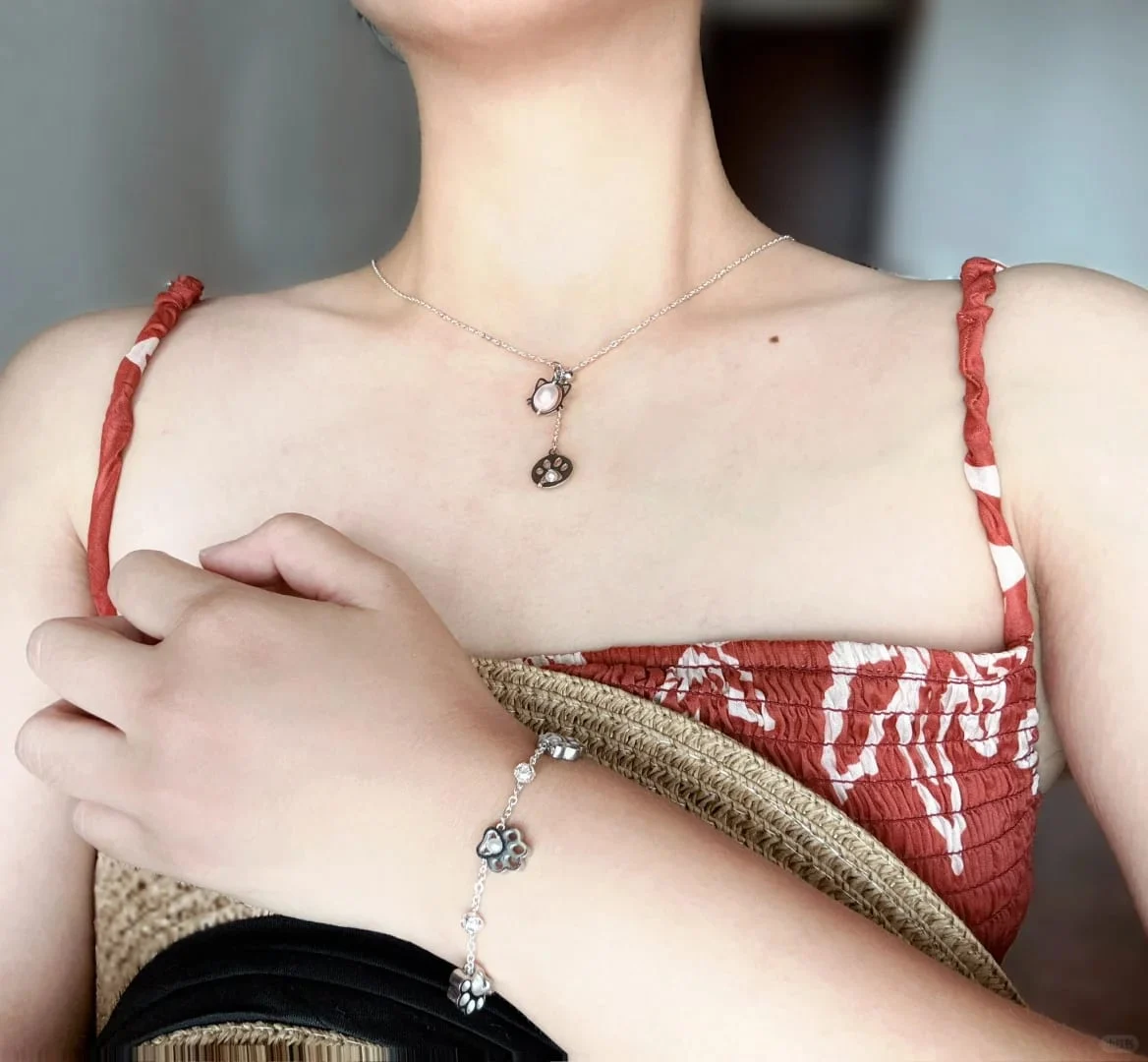 Model in a red patterned strap dress wearing the silver-toned cat and paw drop necklace, with a silver-toned paw-bead bracelet on the wrist.