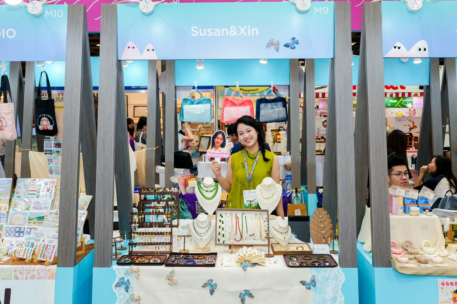 The Susan&Xin jewellery stand beneath a blue and pink sign at the Hong Kong exhibition.